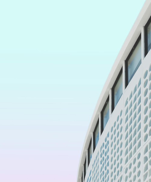 Modern building facade showcasing unique geometric patterns against a pastel sky.